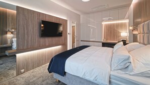 A modern bedroom with a large bed, a flat-screen TV mounted on a wooden panel, a bedside table with a lamp, and a wardrobe with sliding doors. - Hraniční zámeček (Lednice)