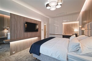 Un dormitorio moderno con una cama grande, un televisor de pantalla plana montado en un panel de madera, una mesita de noche con lámpara y un armario con puertas correderas.