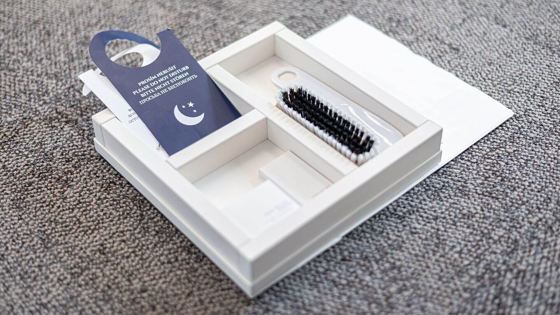 Une boîte blanche contenant un pinceau noir et blanc, une étiquette bleue avec du texte et une carte blanche.