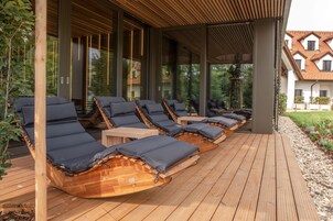 Un área de descanso al aire libre techada, con tumbonas de madera y una terraza de madera.