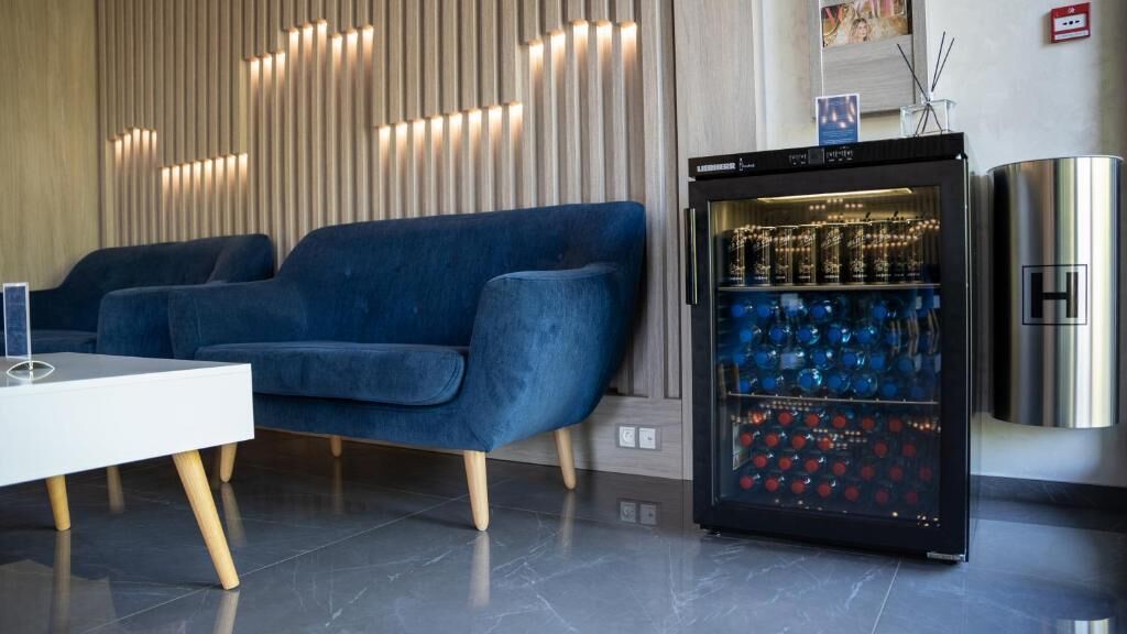 Una sala de estar moderna con un sofá azul, una mesa blanca y un minibar con botellas.