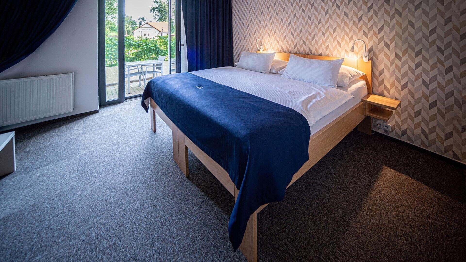 Habitación de hotel con cama, mesita de noche, ventana con cortinas y pared con estampado.