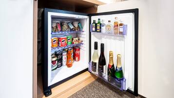 Un refrigerador pequeño con refrigerios, bebidas en lata y botellas de alcohol.