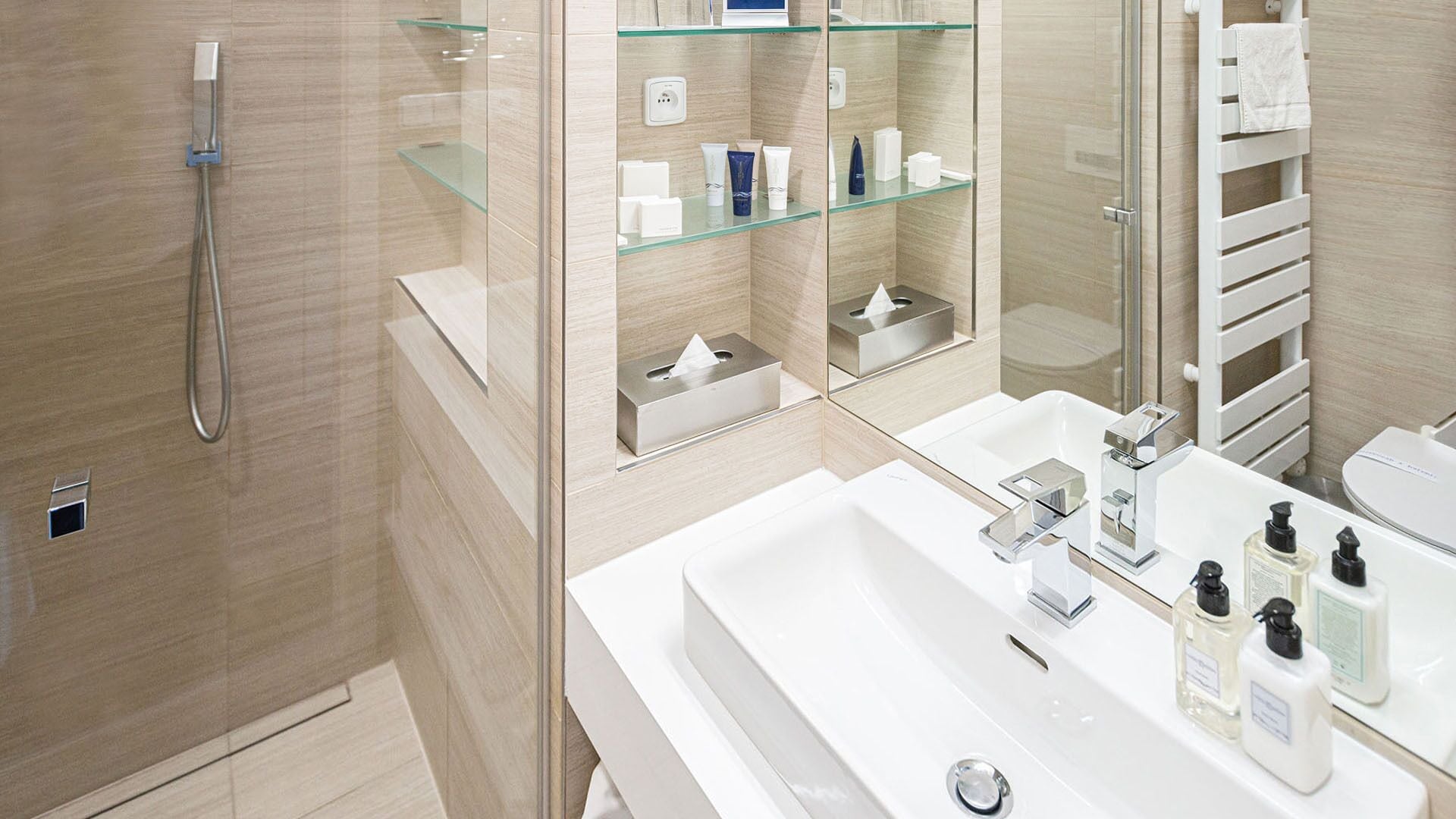 A modern bathroom with a glass shower enclosure, a white sink with chrome fixtures, and a mirrored vanity with glass shelves.