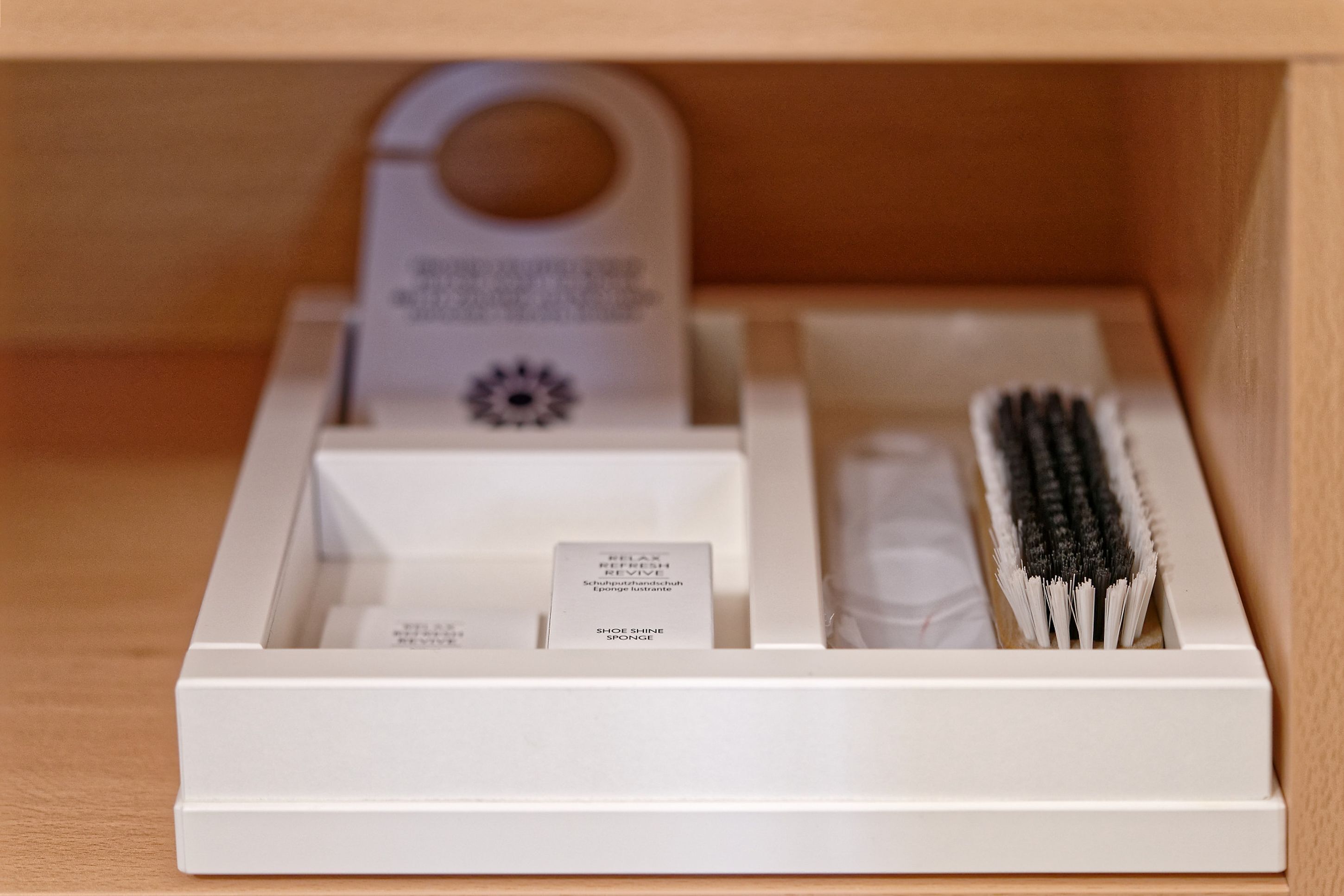 A white shoe shine kit with a brush, sponge, and a label inside a wooden drawer.