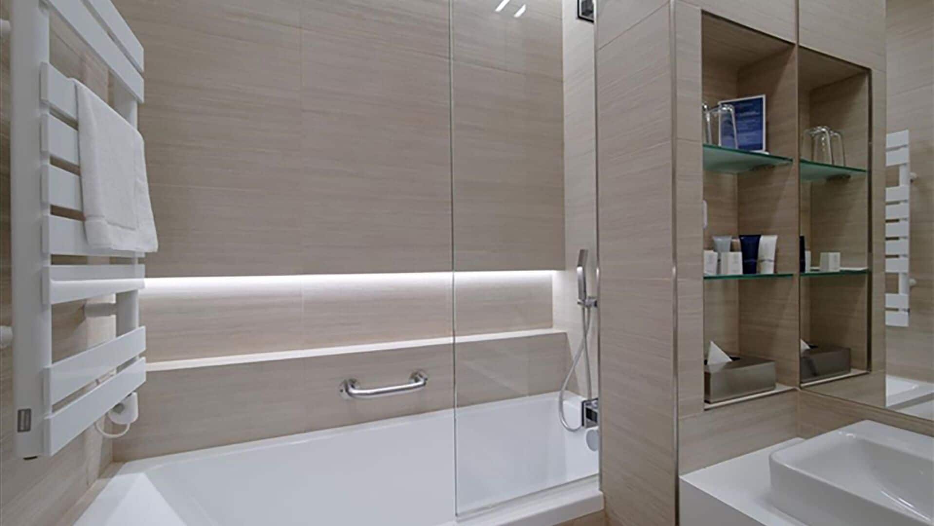 Ein modernes Badezimmer mit einer Badewanne, einer Duschkabine aus Glas und einem Waschtisch mit Regalen.
