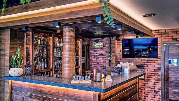 A bar area with a wooden counter, shelves with bottles, and hanging plants. - Hotel Classic (Rzeszów)
