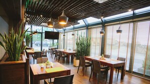 A restaurant with wooden tables and chairs, potted plants, and hanging pendant lights. - Hotel Classic (Rzeszów)