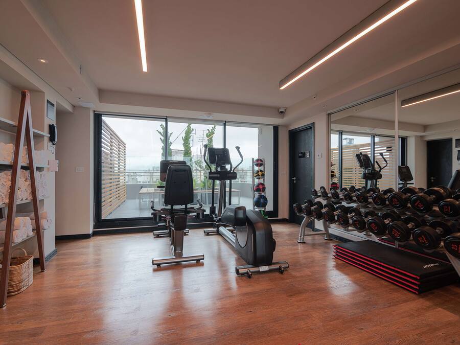 A modern gym with cardio machines, dumbbells, and a large mirror.