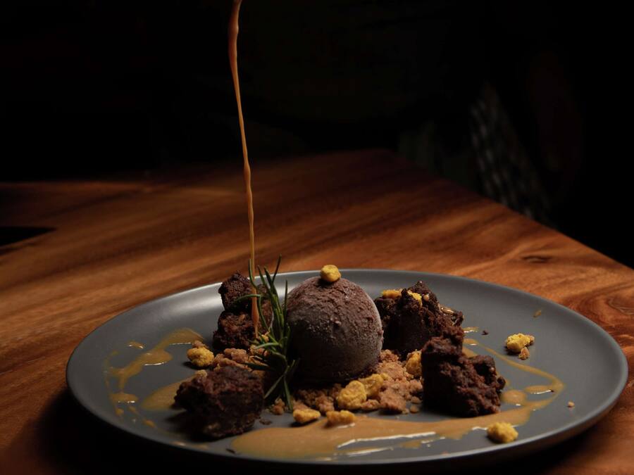 Un plato de postre con una porción de helado y una cuchara sirviendo salsa.
