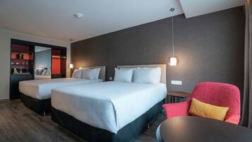 A hotel room with two beds, a red armchair, a small table, and a mirror.