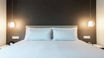 Una cama bien hecha con ropa blanca, dos lámparas de noche y un enchufe en la pared.