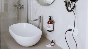 A bathroom with a white sink, a glass shower enclosure, a round mirror, and a hairdryer mounted on the wall.
