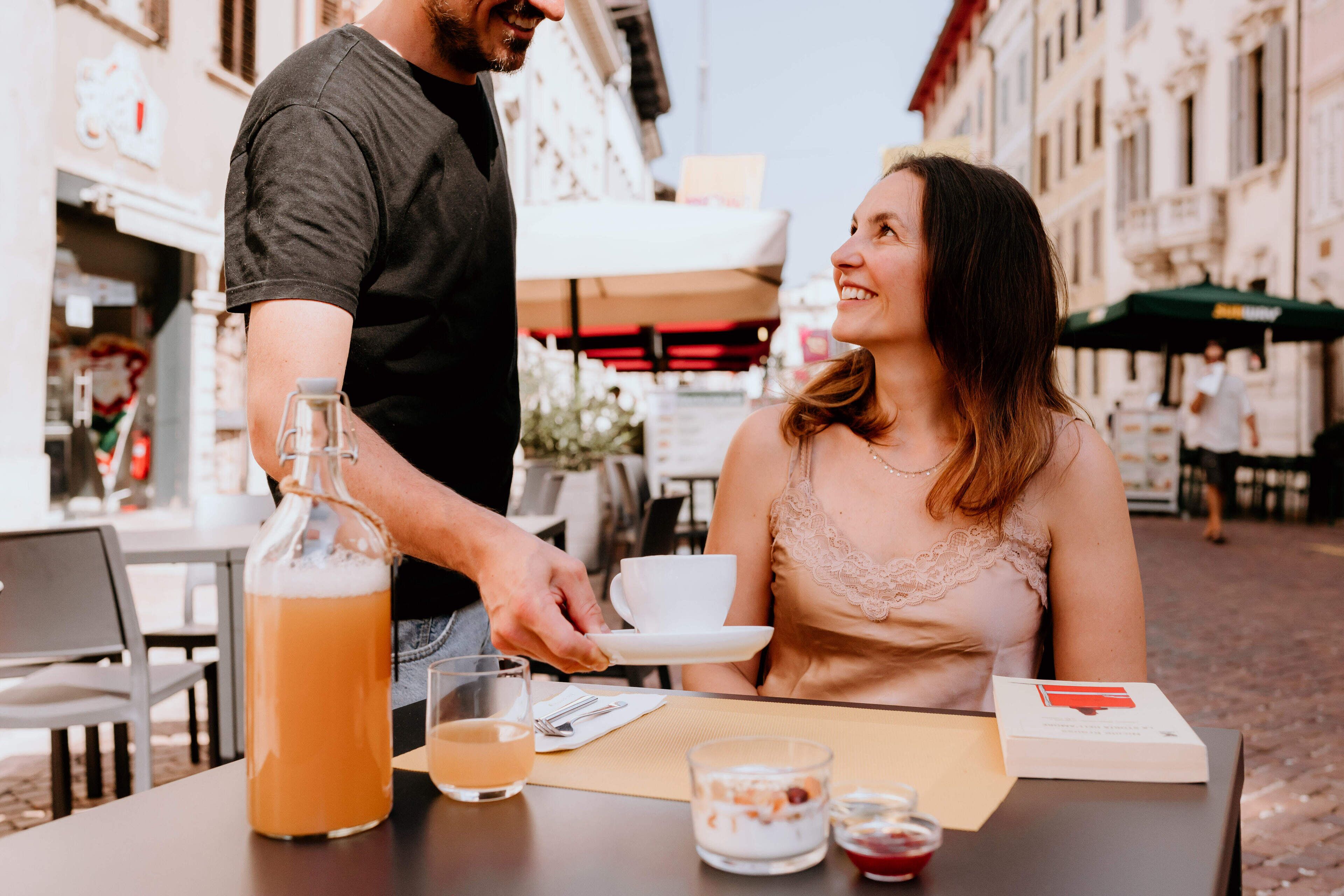Ein Paar sitzt in einem Straßencafé an einem Tisch für zwei, mit einem Getränk, einem Glas und einer Speisekarte.