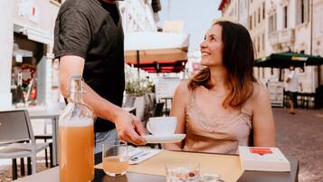 Um casal sentado em um café ao ar livre, com uma mesa posta para dois, incluindo uma garrafa de bebida, um copo e um cardápio.