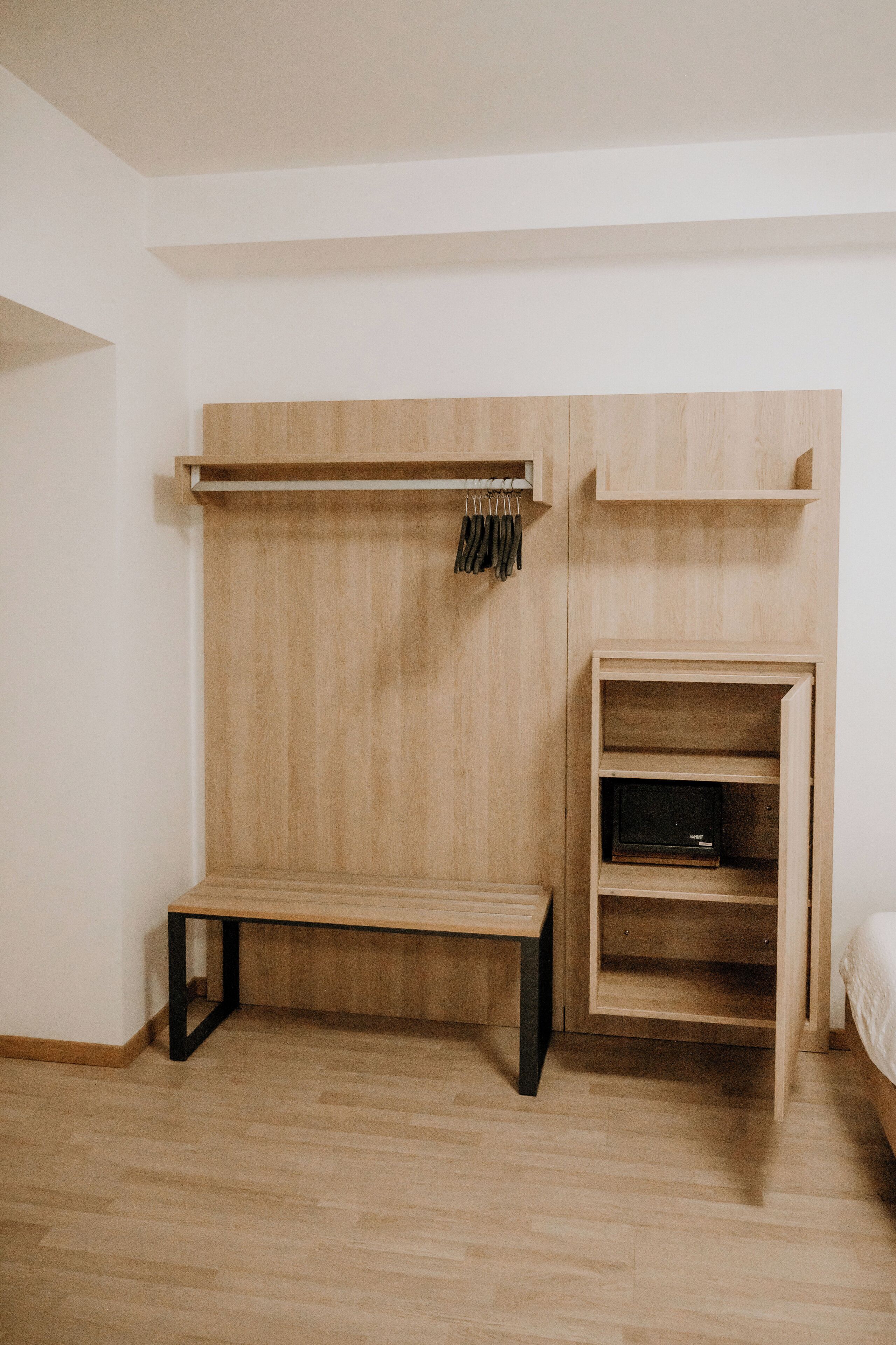 A minimalist room with a wooden bench, a coat rack, and a built-in shelving unit.
