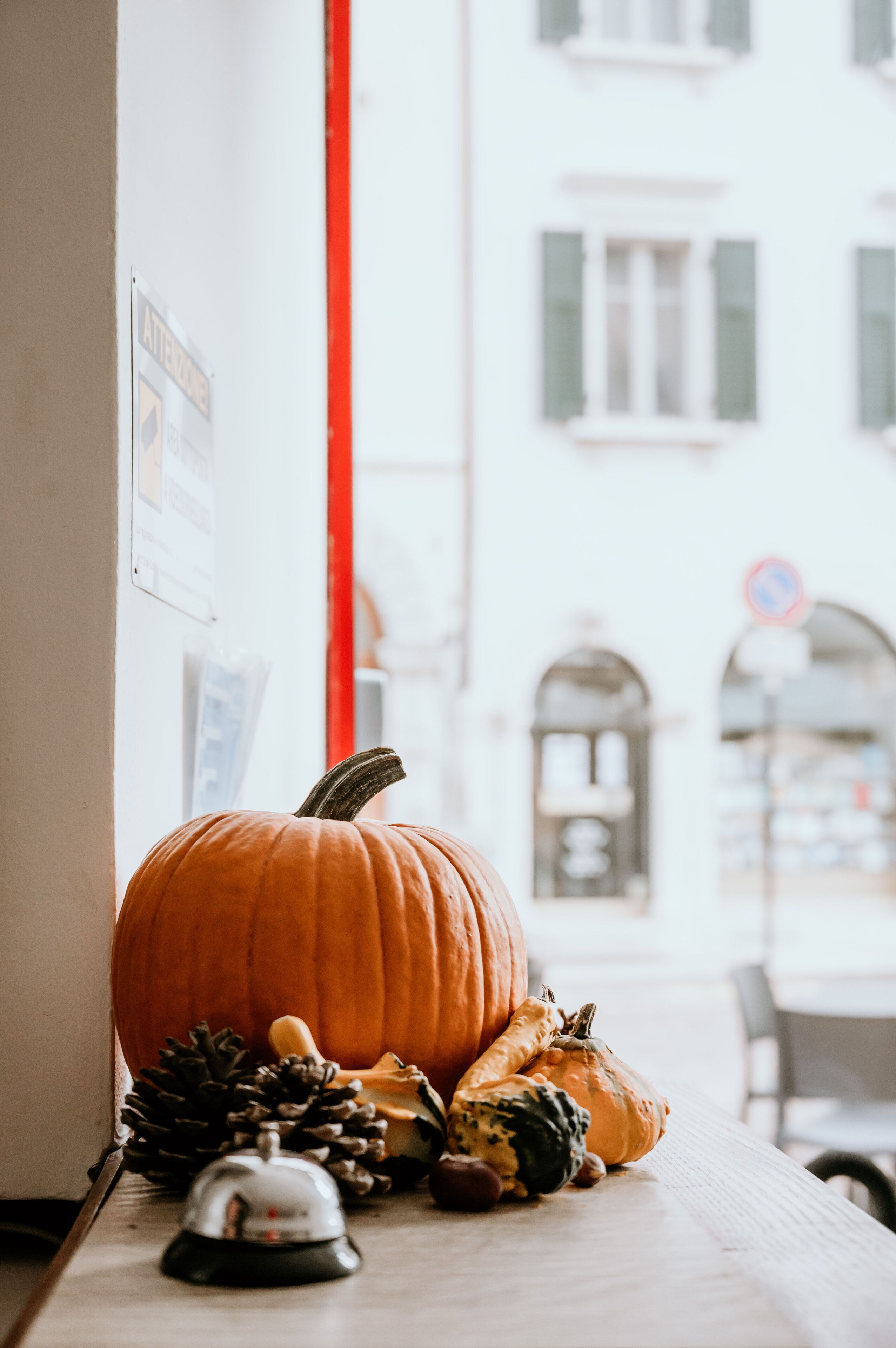 A pumpkin and other autumn decorations on a table near a window with a view of buildings.