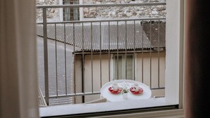 Ein Balkon mit Tisch für zwei Personen, mit Blick auf ein Steinhaus mit Fensterläden.