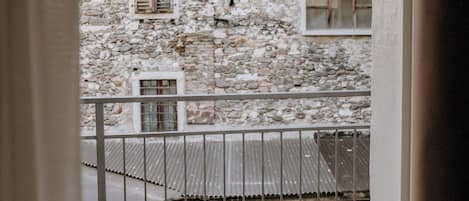 A balcony with a table set for two, overlooking a stone building with shutters.