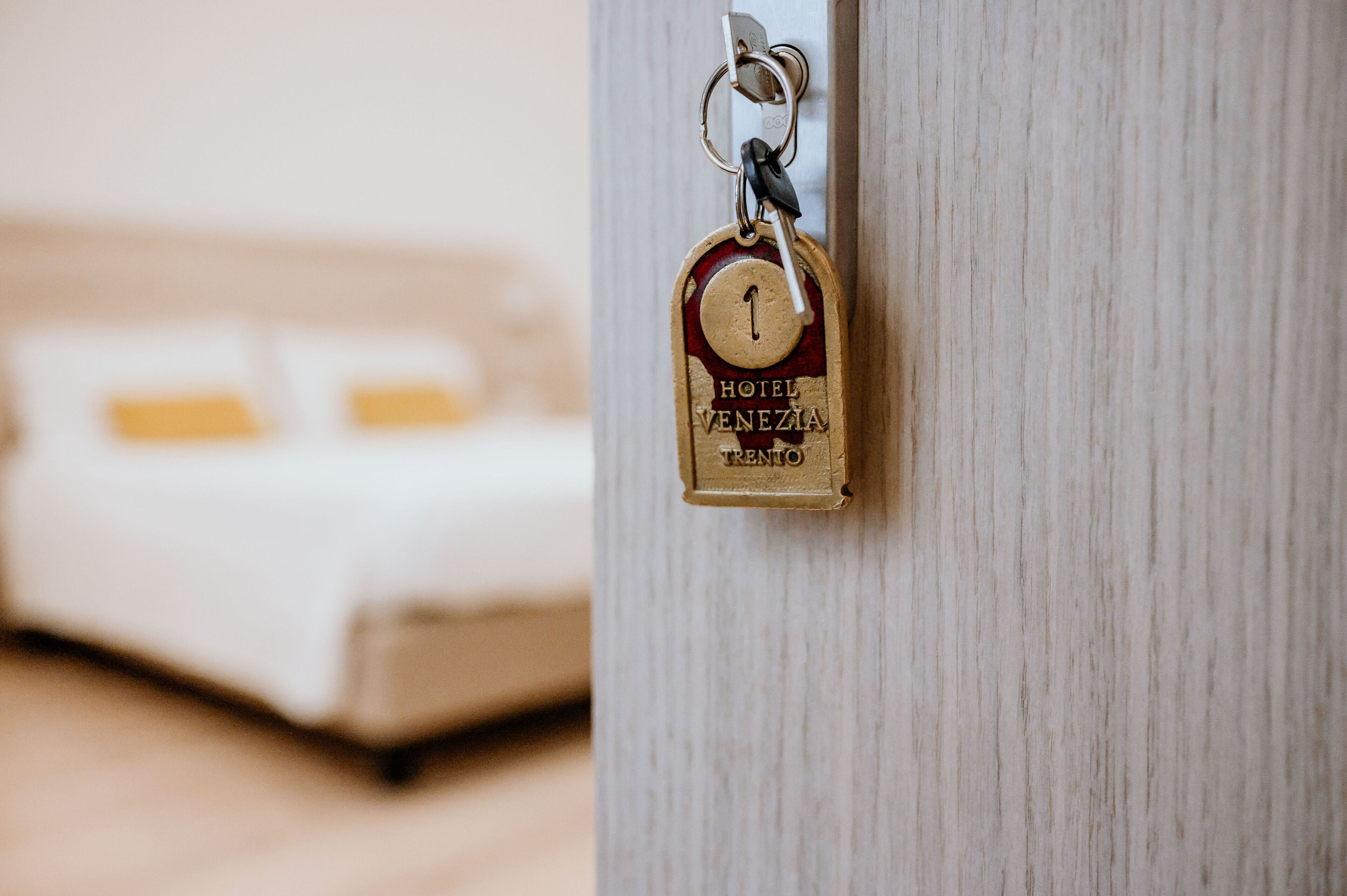 Ein Schlüssel mit Vorhängeschloss an einer Holztür, im Hintergrund ein verschwommenes Bett.