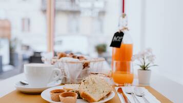 A breakfast setting with a white cup, a plate with bread and pastries, a glass of orange juice, and cutlery on a table.