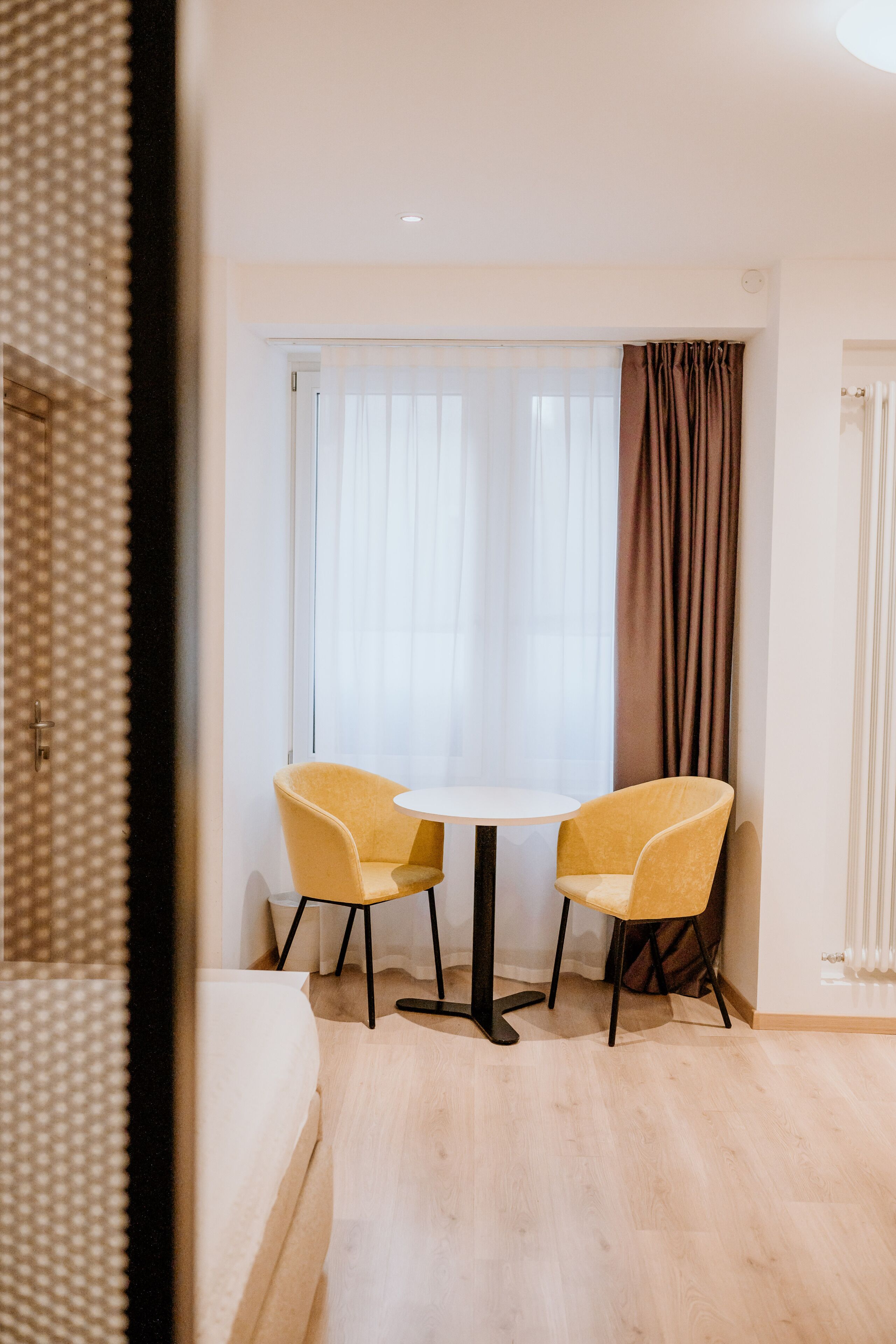 A hotel room with a bed, a round table, two chairs, and a window with curtains.