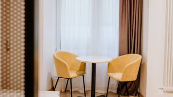 A hotel room with a bed, a round table, two chairs, and a window with curtains.