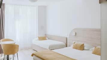 Ein modernes Hotelzimmer mit zwei Betten, einer Sitzecke mit einem Sessel und einem großen Fenster.