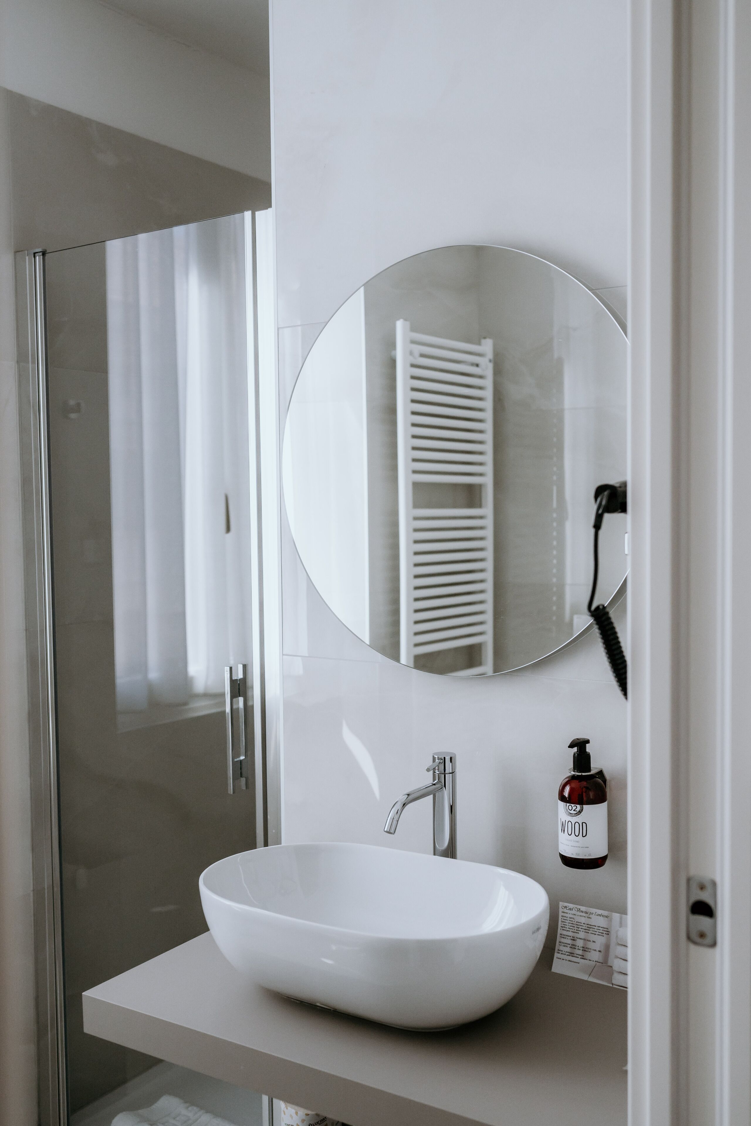 A modern bathroom with a white sink, a round mirror, and a glass shower enclosure.