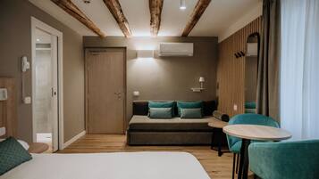 A modern hotel room with a large bed, a sofa, two chairs, a small table, wooden beams on the ceiling, and a door.