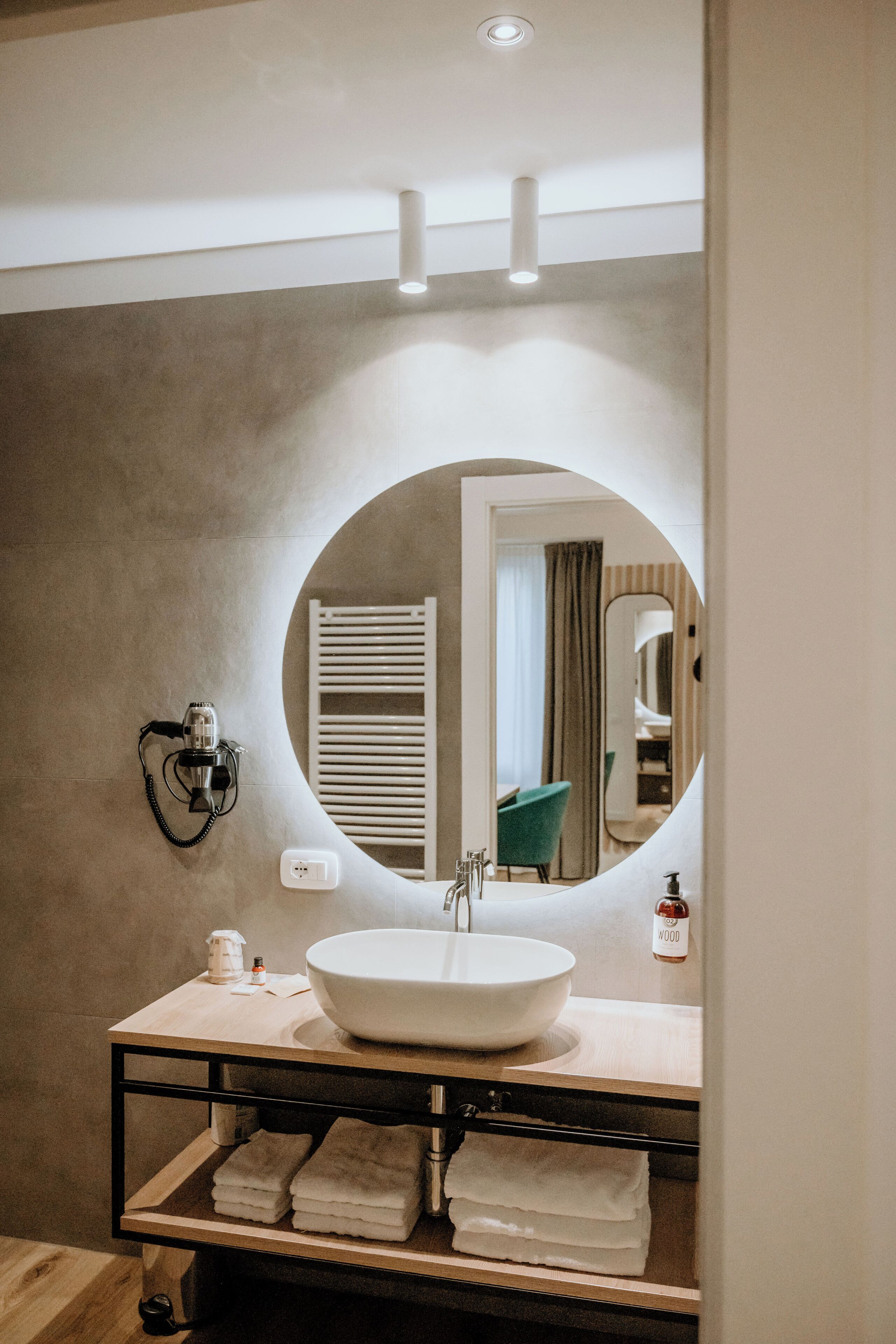 Une salle de bain avec un miroir rond, un lavabo, un porte-serviettes et un sèche-cheveux fixé au mur.