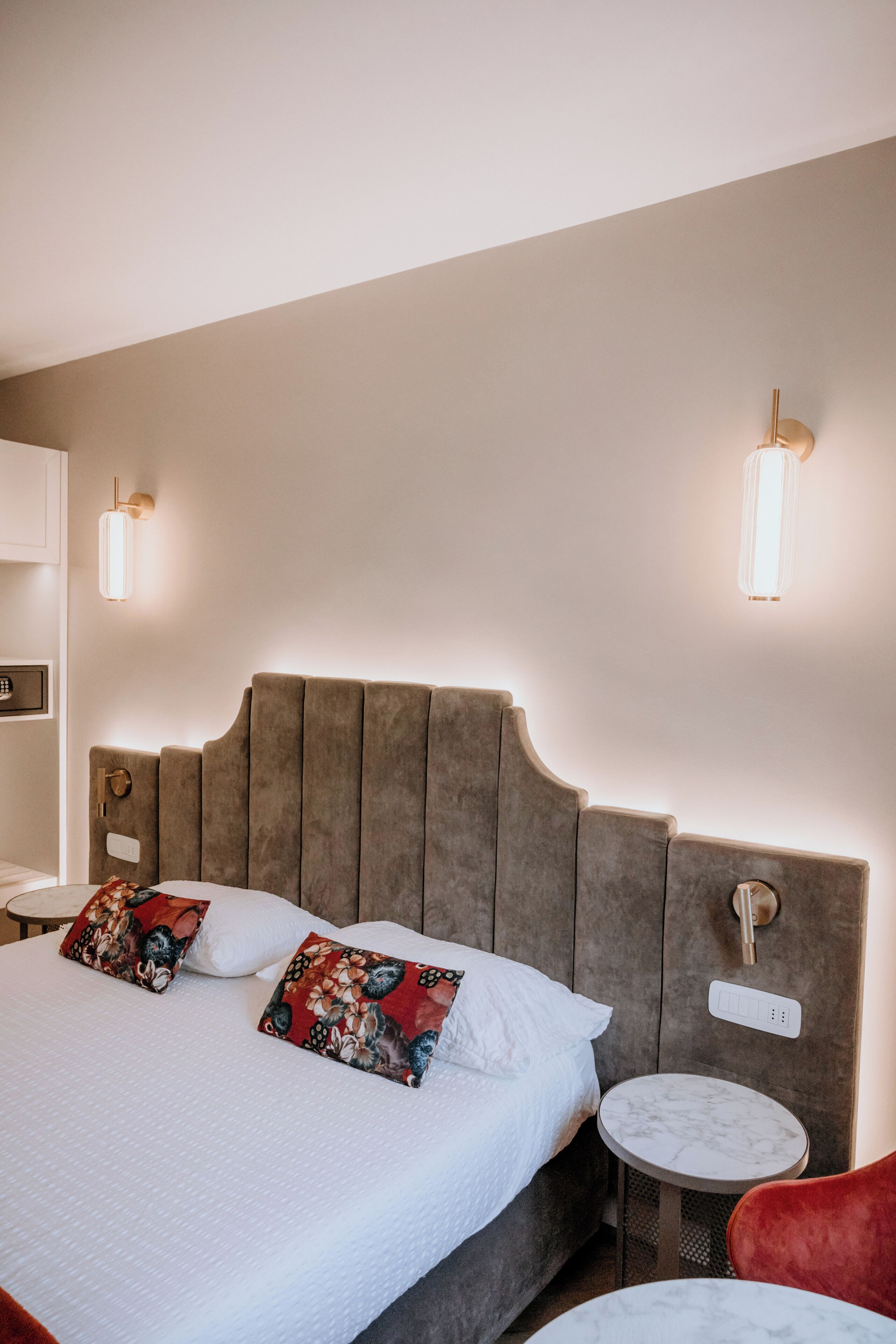 Una habitación de hotel con una cama grande, dos mesitas de noche, una silla roja y una pequeña mesa redonda.