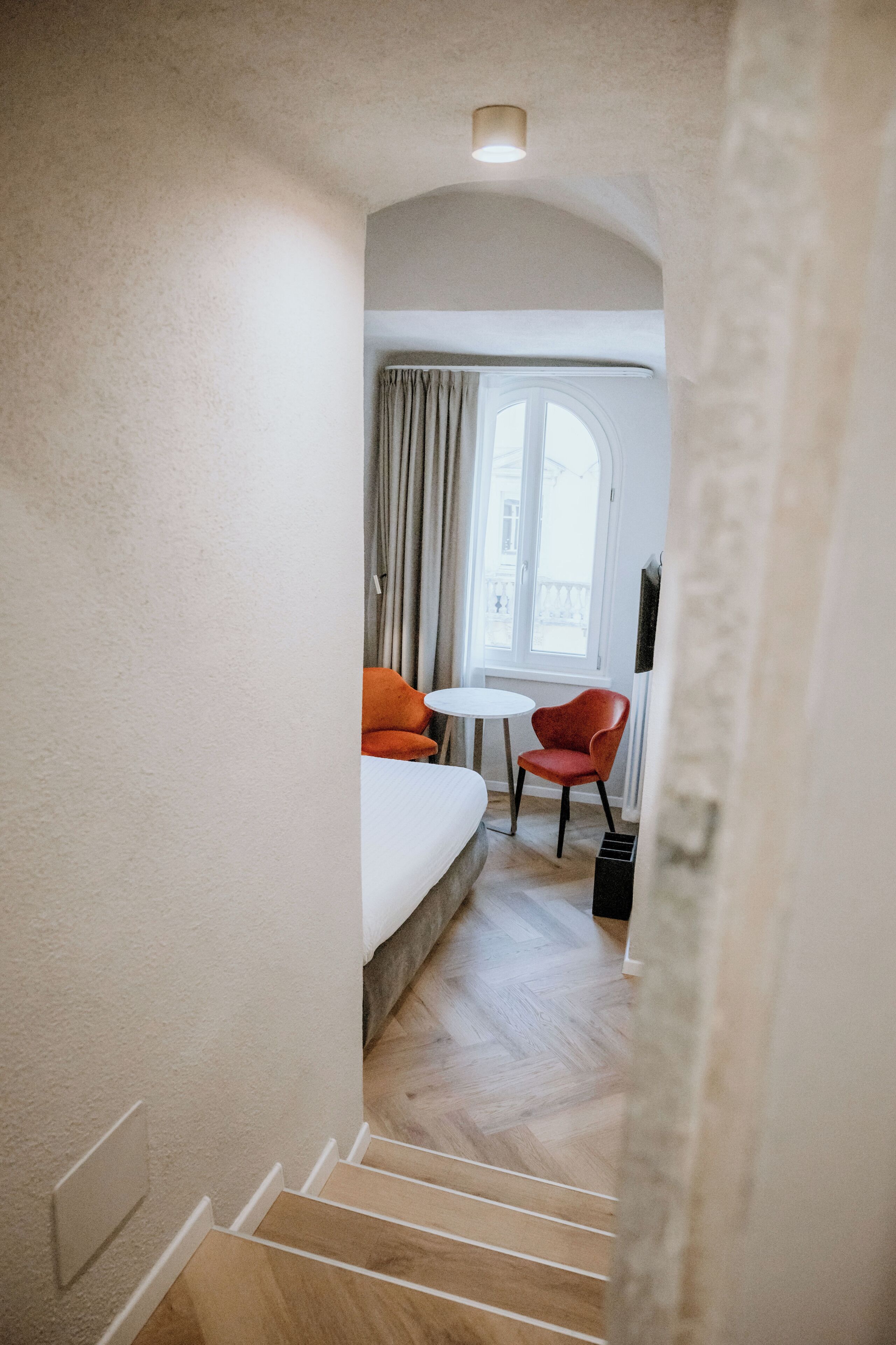 Habitación de hotel con cama, una mesita, dos sillas y un ventanal con cortinas.