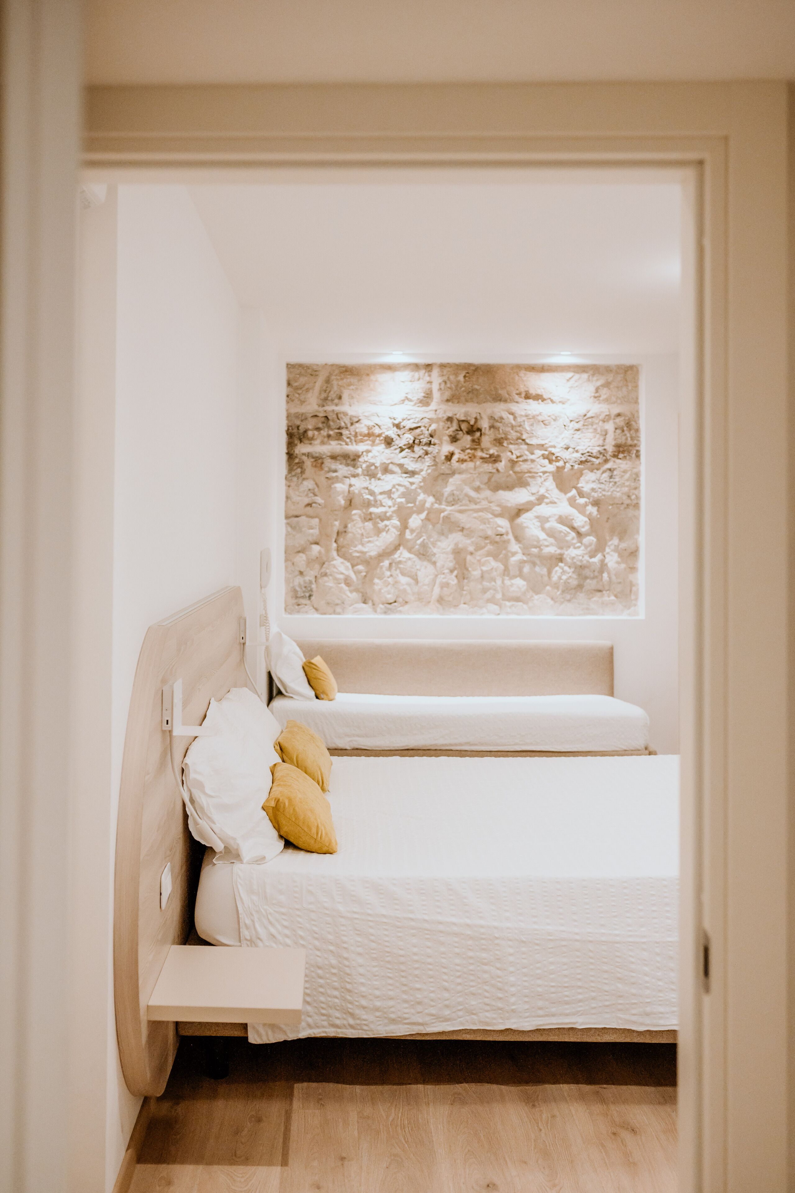 A small, white, single-bed room with a stone wall mural above the bed and a wooden floor.