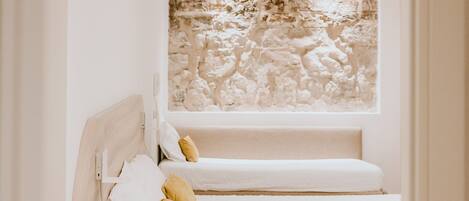 A small, white, single-bed room with a stone wall mural above the bed and a wooden floor.