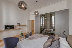Un dormitorio moderno con una cama grande, un televisor en un estante, una silla y un escritorio.