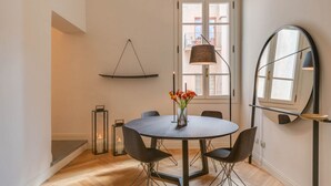 A modern dining area with a round table, black chairs, a vase with flowers, a hanging lamp, and a mirror on the wall. - Apartments Florence Giotto Deluxe (Firenze)