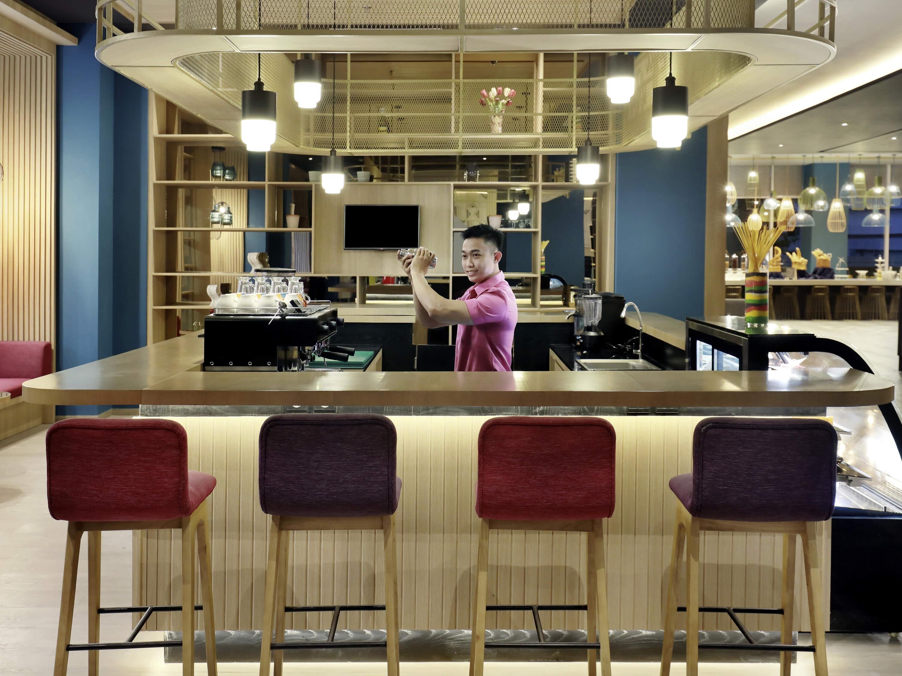 A modern bar area with a counter, stools, and a person pouring a drink.