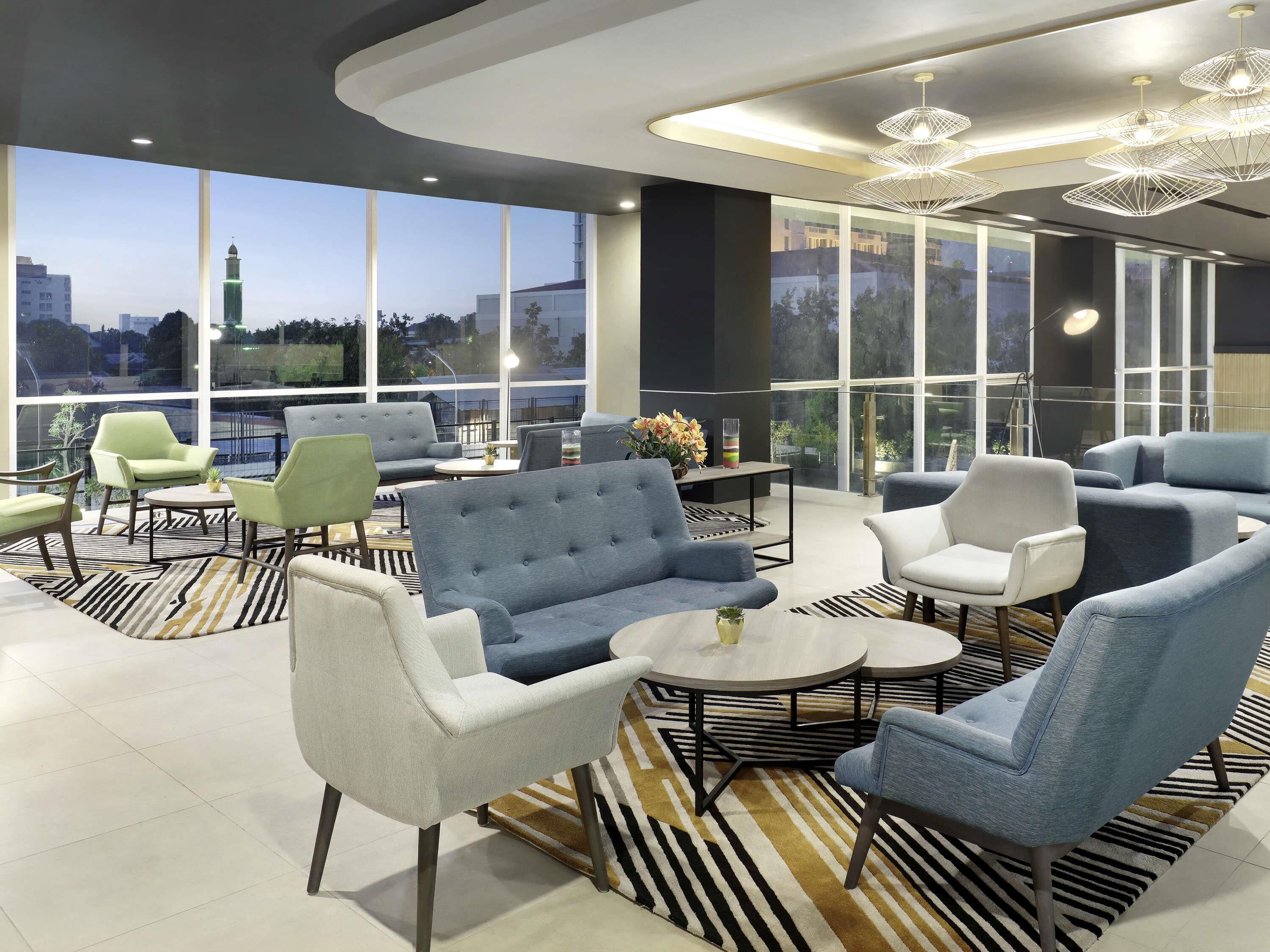 A modern lounge area with sofas, chairs, and a coffee table, large windows offering a view of the cityscape.