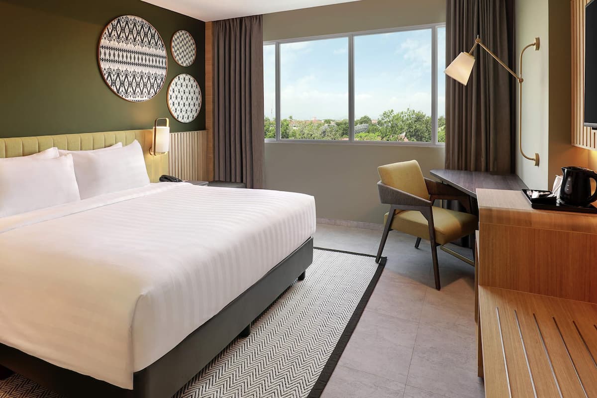 Ein Hotelzimmer mit einem großen Bett, einem Schreibtisch, einem Sessel, einer Kaffeemaschine und Blick ins Freie.