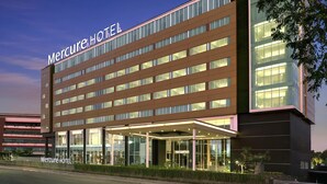 A modern hotel building with a prominent 'Mercure Hotel' sign, large windows, and a well-lit entrance area.