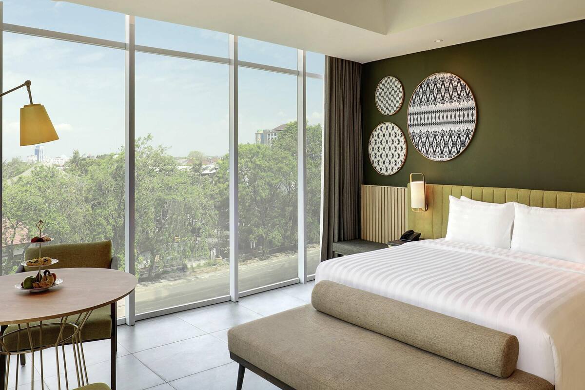 Ein Hotelzimmer mit einem großen Bett, einem Esstisch und Blick auf Grünflächen.
