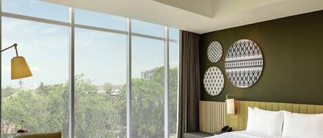 A hotel room with a large bed, a dining table, and a view of greenery.