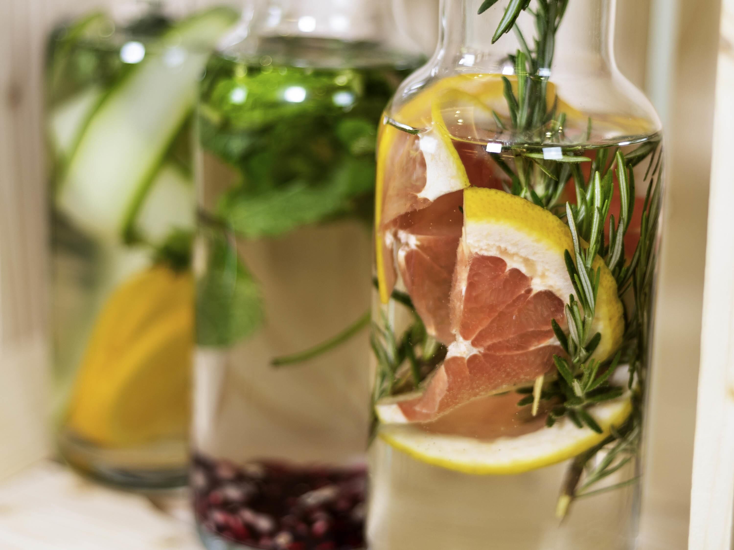 Three glass bottles with herbs and citrus slices.