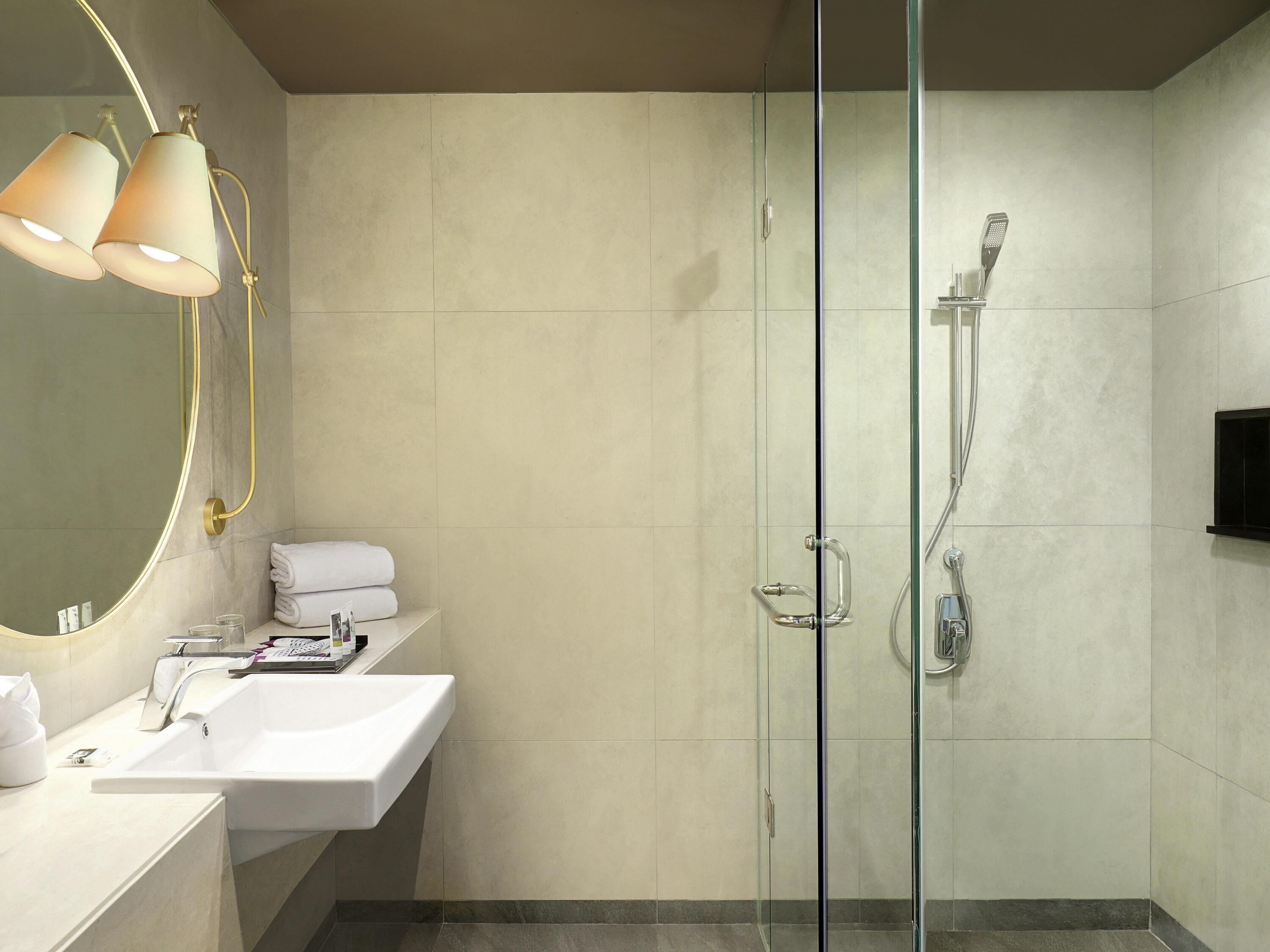 Un baño moderno con ducha envuelta en vidrio, un lavamanos blanco y un espejo con dos luces colgantes.