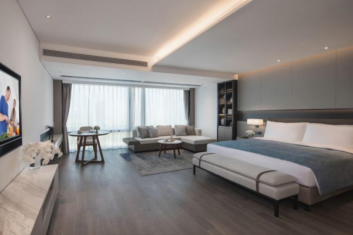 A modern hotel room with a large bed, a sofa, a small table, and a TV.