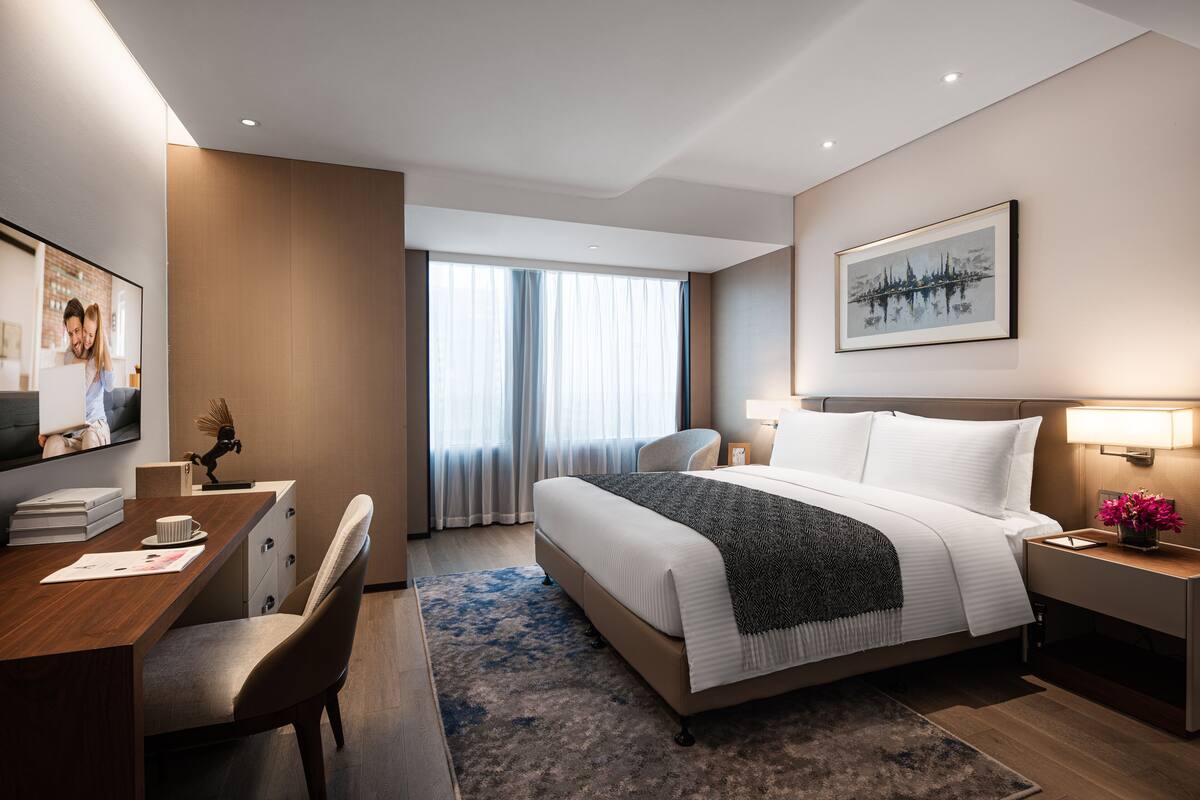 Une chambre d’hôtel moderne, dotée d’un grand lit, d’un bureau, d’une chaise, d’une table de chevet et d’une fenêtre avec des rideaux.