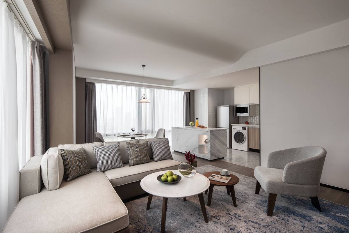 Une chambre d’hôtel moderne équipée d’un canapé, d’une table à manger, d’un coin cuisine et d’un petit fauteuil.