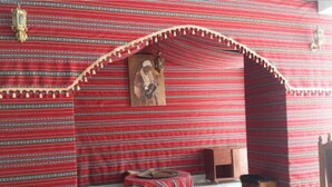 Une pièce avec un mur rouge à motifs, un banc en bois, une petite table et un tableau encadré accroché au mur.