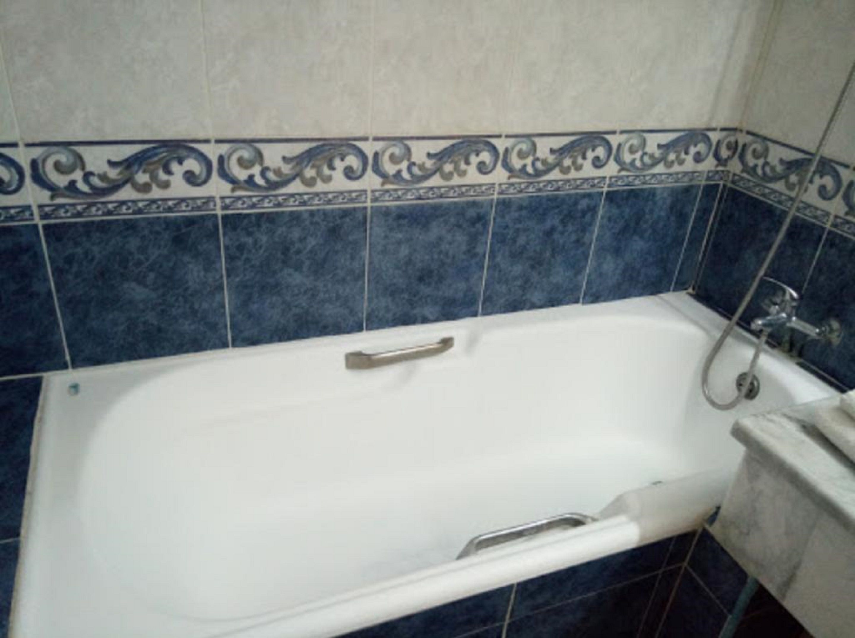 Un bany amb banyera blanca, rajoles blaves i zona de dutxa.